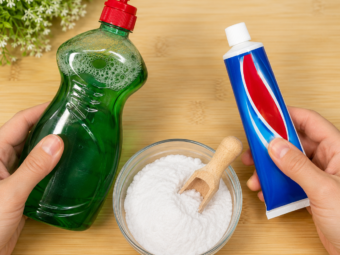 Hände halten eine Flasche Spülmittel und eine Tube Zahnpasta neben einer Schüssel mit Natron auf einer Holzoberfläche als Hausmittel für verschiedene Reinigungsaufgaben im Haushalt.